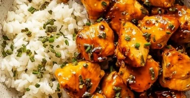 A bowl of hot honey chicken with rice and colorful vegetables