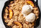 Delicious Smoked Bourbon Peach Cobbler topped with whipped cream in a baking dish